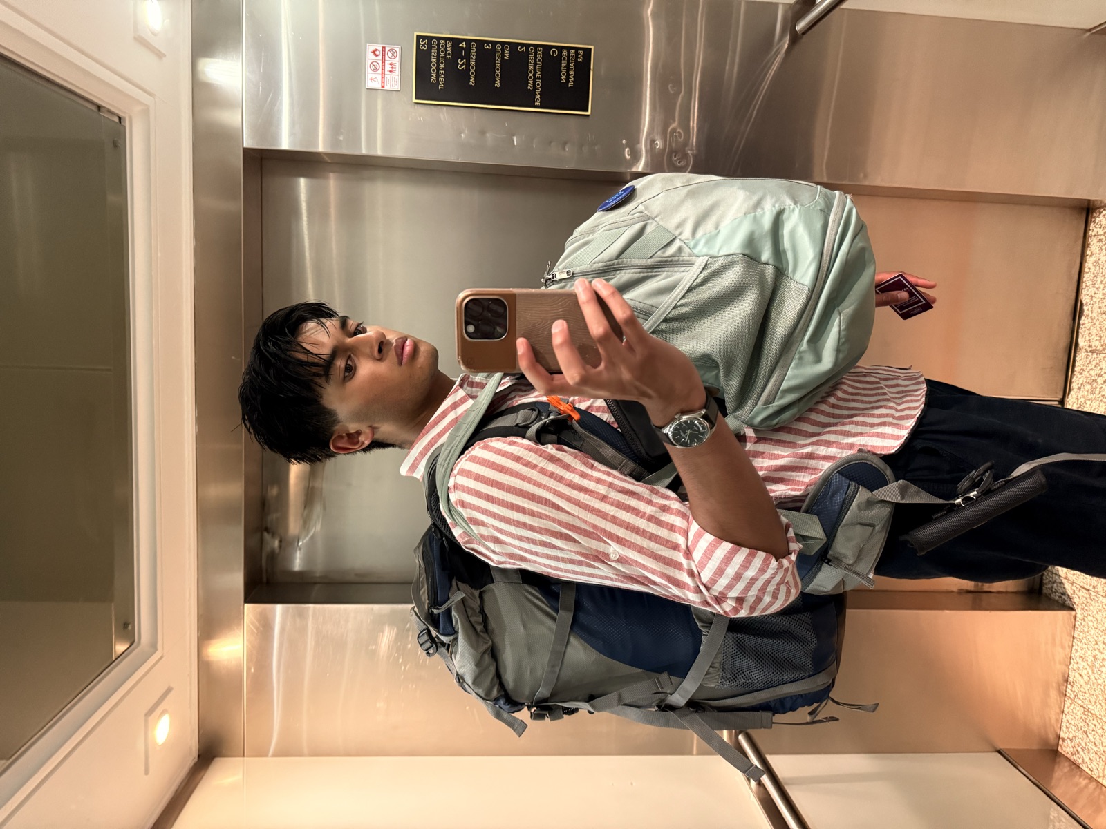 Ariyan in an elevator mirror carrying a huge hiking backpack on his back and a second pack on his front