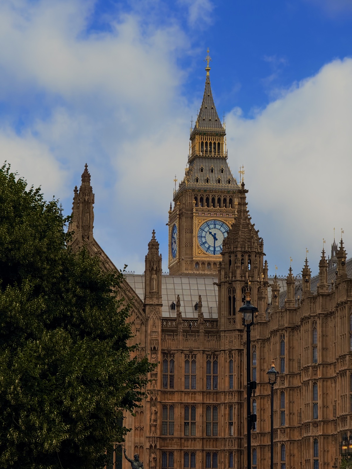Big Ben's gilded clock face and spire rising over the Gothic stonework of the Palace of Westminster