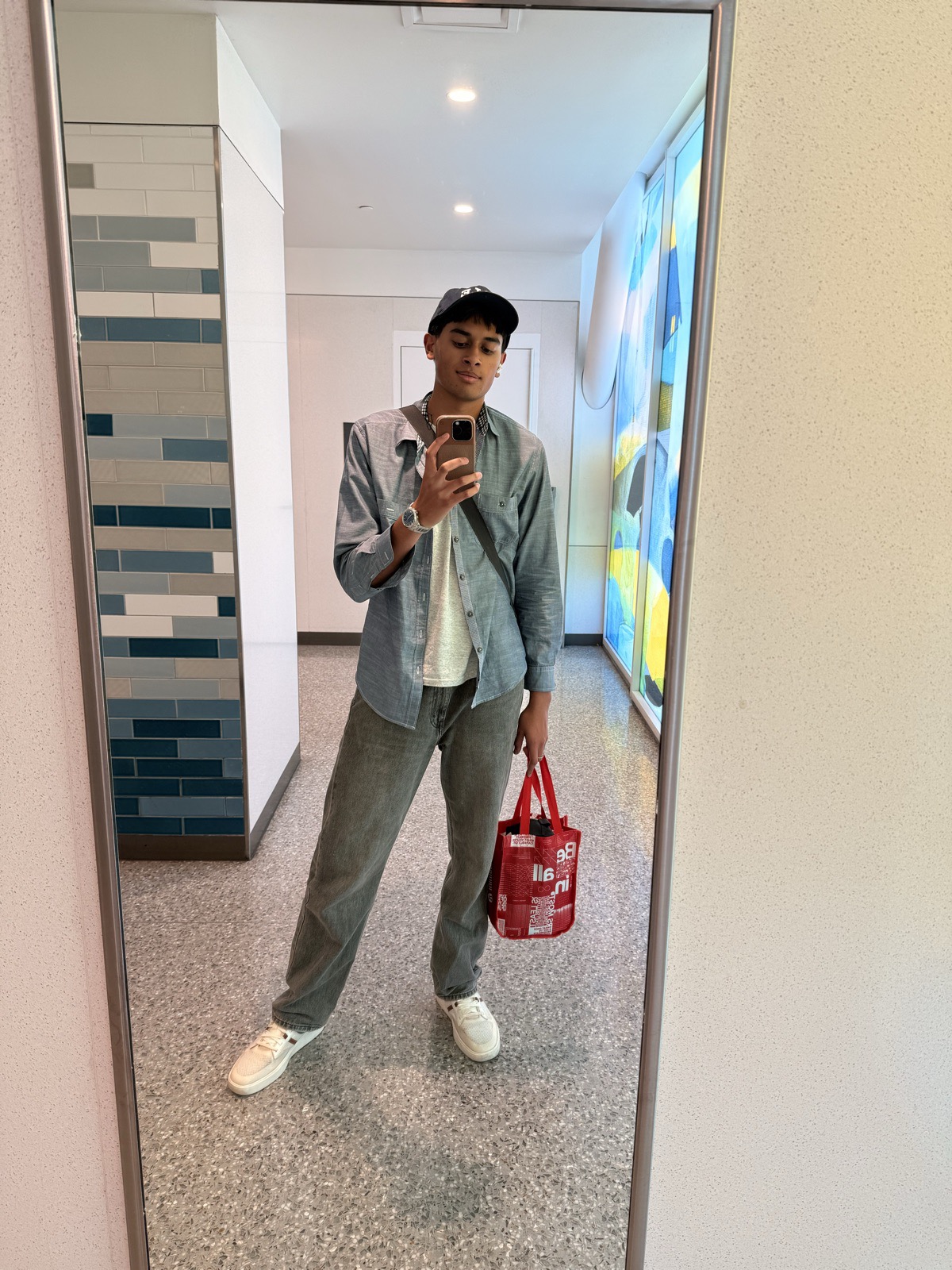 Ariyan in a mirror selfie with a cap and crossbody bag, holding a red tote, off to pitch