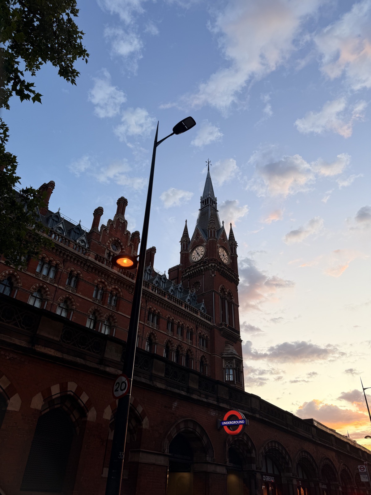 St Pancras station's Gothic red brick clock tower silhouetted against a pastel sunset with an Underground roundel glowing below