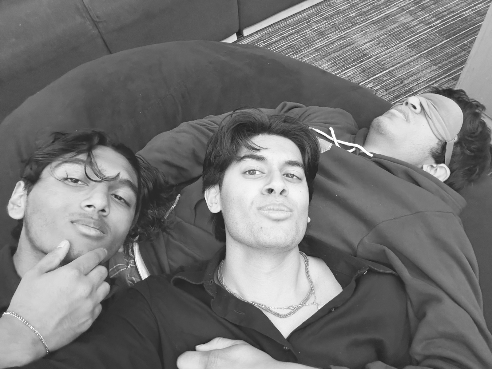 Black-and-white selfie of Ariyan and two friends collapsed on a beanbag, one asleep in an eye mask